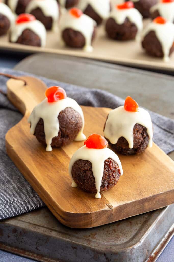 Three mini Christmas puddings sit on a small wooden platter, with a tray in the background.