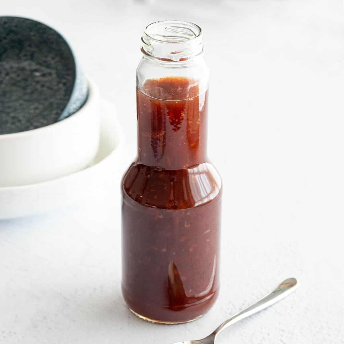 Bottle of Worcestershire sauce with spoon and bowls in background.