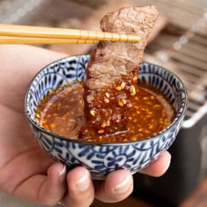 A pair of chopsticks dips a piece of meat into homemade yakiniku sauce.