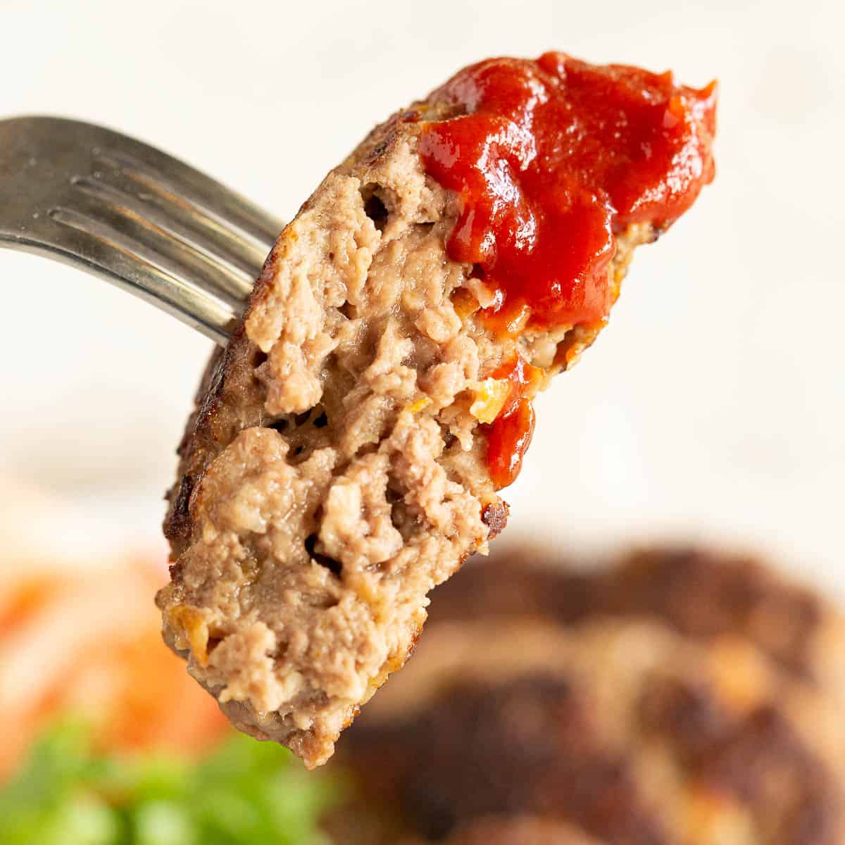 A large juice rissole dipped in tomato sauce on a fork.