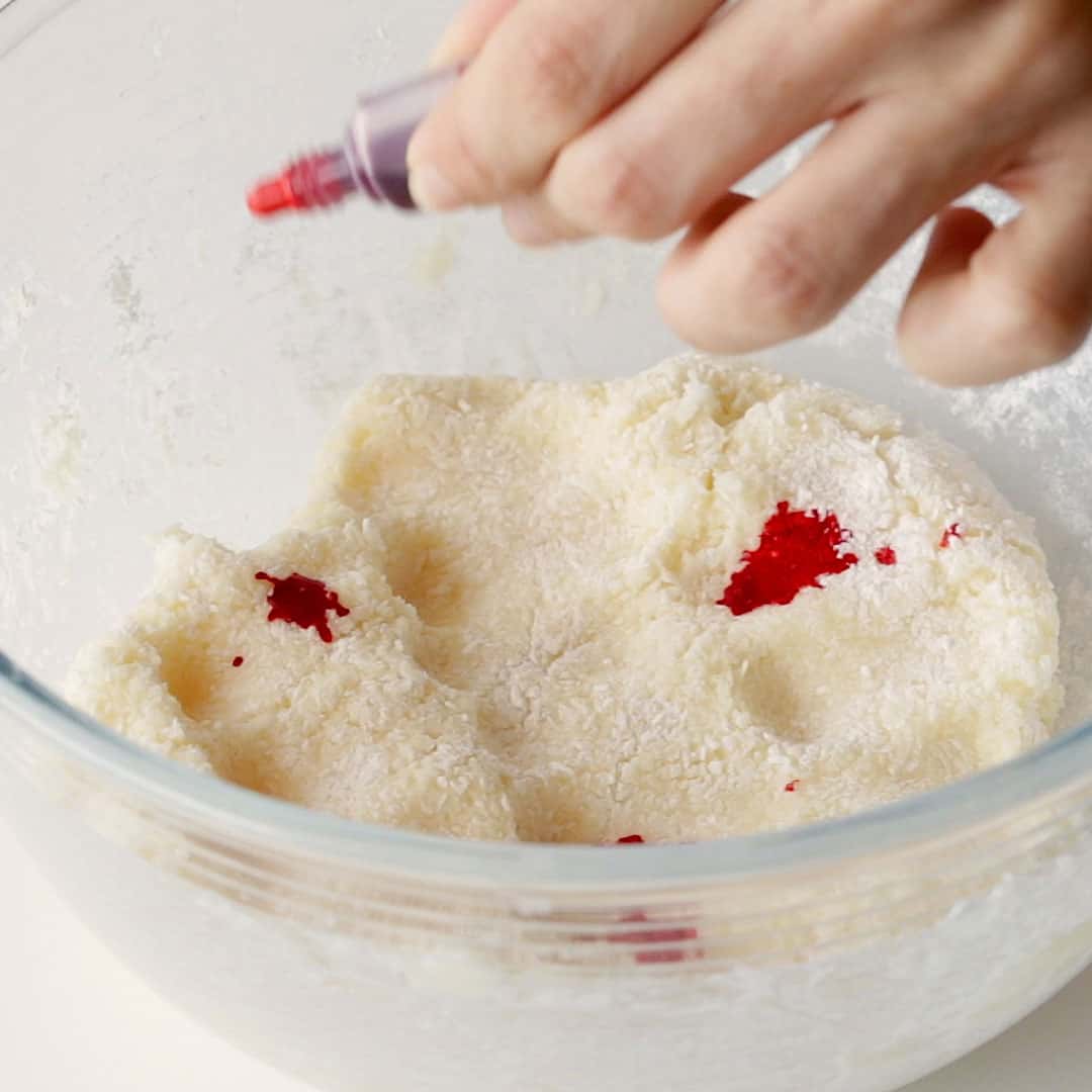 Squeezing drops of red food colouring onto the coconut ice mixture.