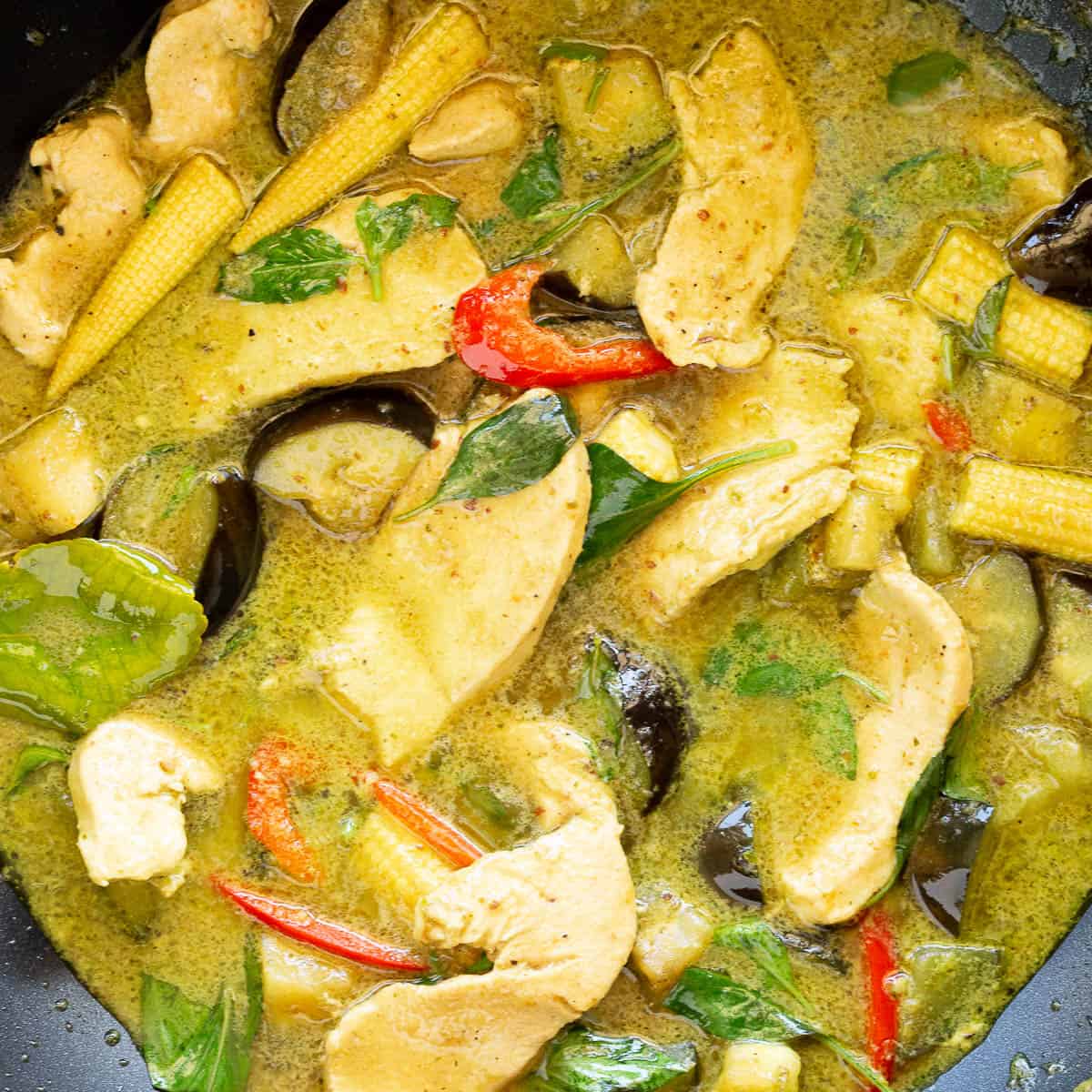 A large wok filled with Thai green chicken curry with eggplant and baby corn.