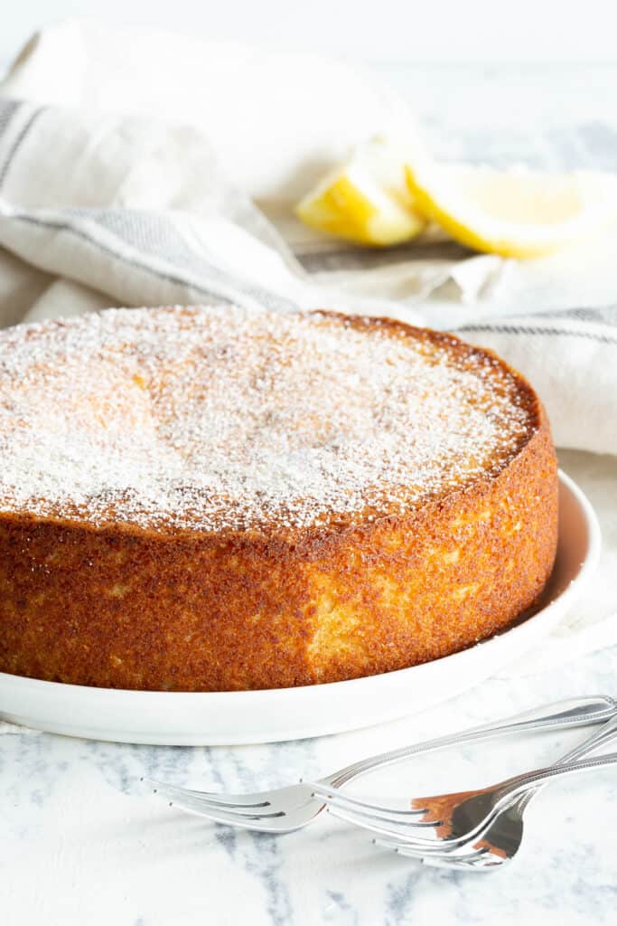 Lemon ricotta cake on a plate showing the golden brown crust, dusted with icing sugar.