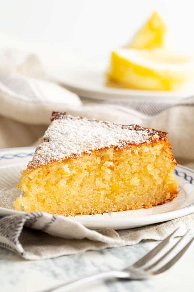 Slice of ricotta cake on a plate with a cake fork in the foreground.