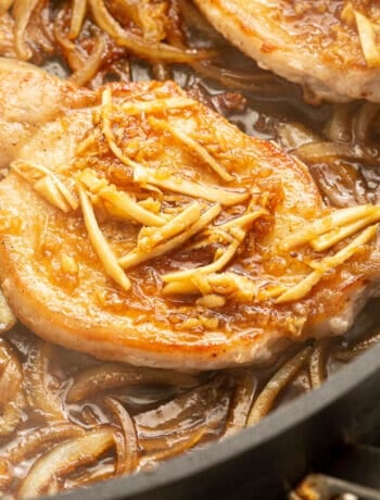 Close up shot of shogayaki cooking in a pan topped with thin slices of ginger.