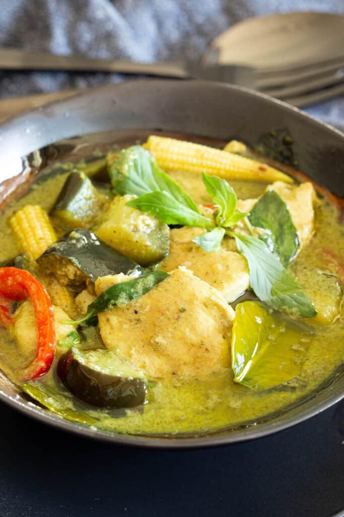 A bowl of Thai green curry with chicken and topped with Thai basil.