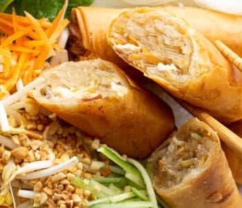 Close up shot of three sliced spring rolls on a bed of cucumber, carrot and peanuts.