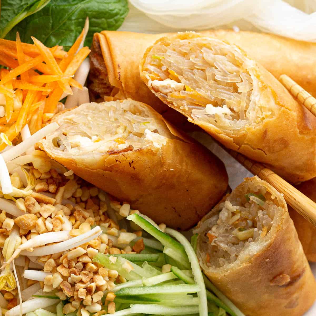 Close up shot of three sliced spring rolls on a bed of cucumber, carrot and peanuts.