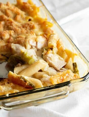 A clear glass baking dish filled with freshly cooked chicken and pasta, with a golden cheesy breadcrumb topping.