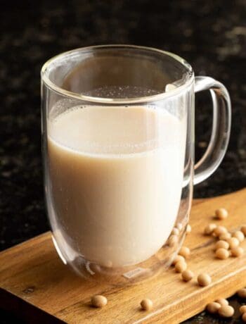 A glass of soy milk on a wooden board with dried soybeans scattered around,