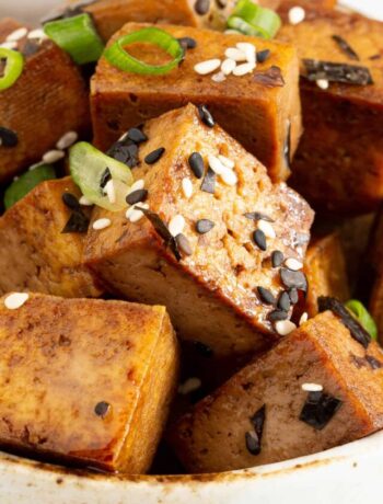 Teriyaki tofu chunks in a bowl sprinkled with sesame seeds and spring onion.