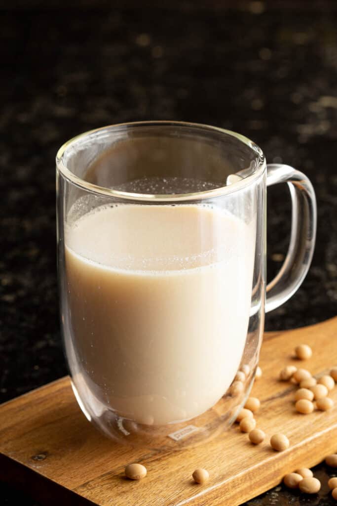 A glass of soy milk on a wooden board with dried soybeans scattered around,