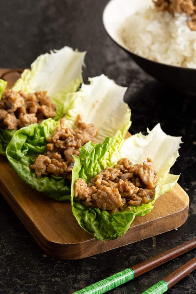 Three lettuce cups filled with nikumiso sit on a wooden board next to chopsticks.