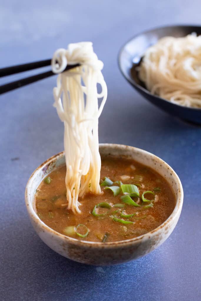 Chopsticks dip ramen noodles into a bowl of tsukemen.