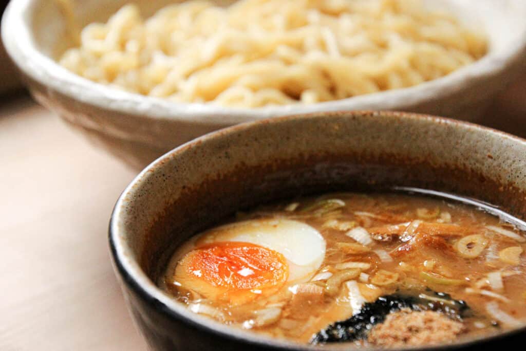 A bowl of tsukemen is topped with half a boiled egg and nori seaweed sheet.