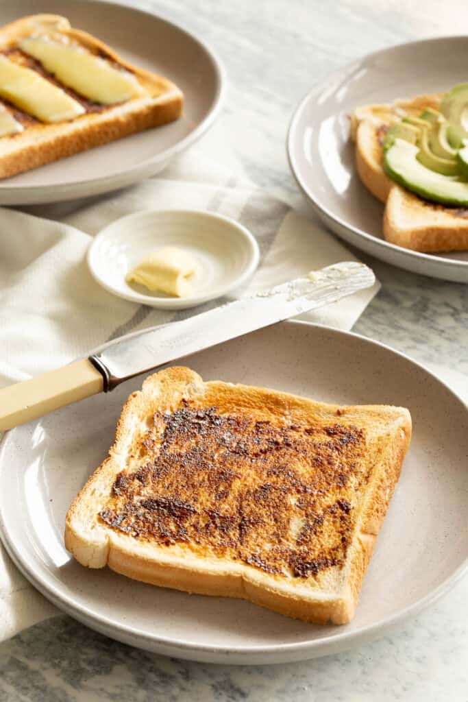 A piece of vegemite on toast with butter and other toast in the background.