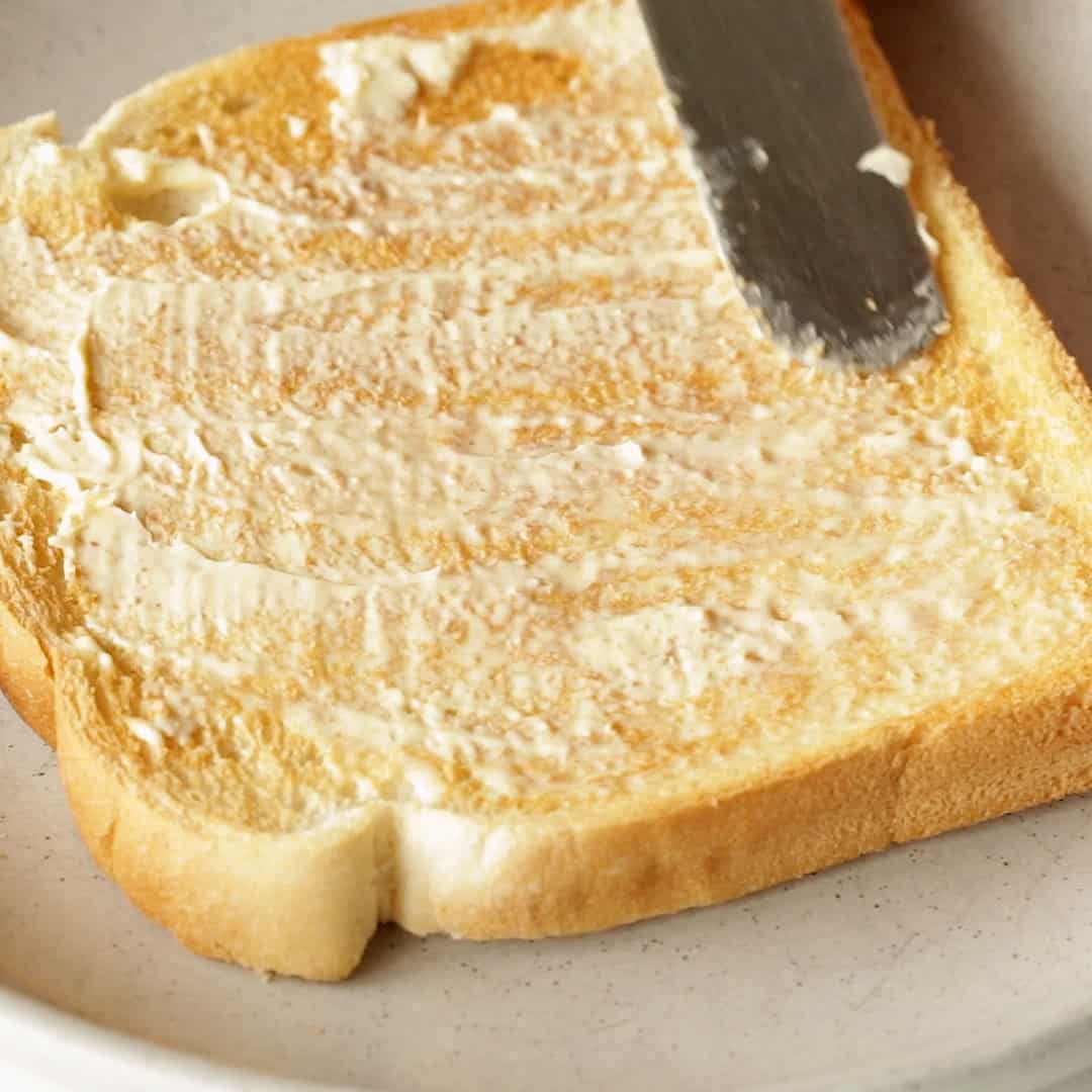 Spreading butter on a slice of white toast.