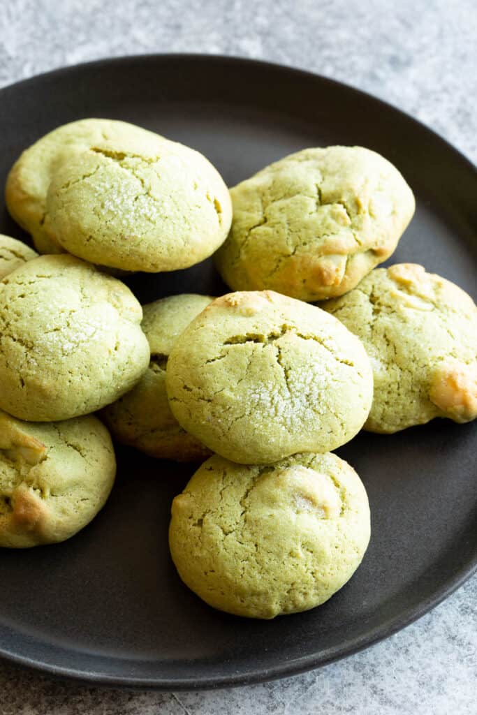 Pile of green matcha cookies on a black plate.