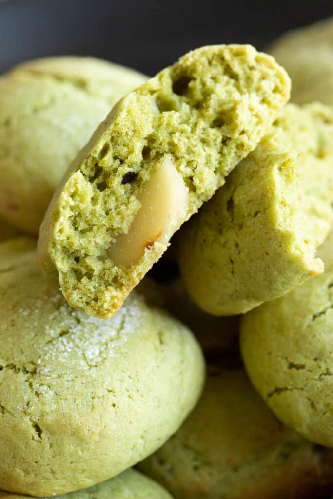A green matcha cookie is broken in half to show the texture and toasted macadamia.