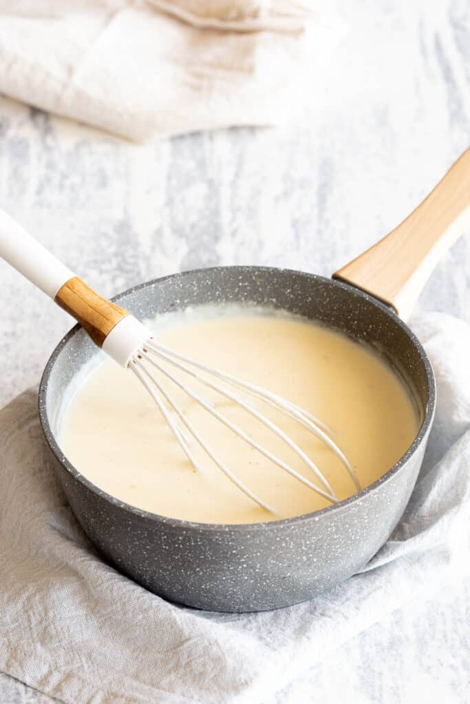 Whisk sitting in a saucepan with white sauce.