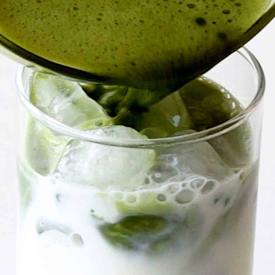 Pouring matcha tea into an iced glass of milk.