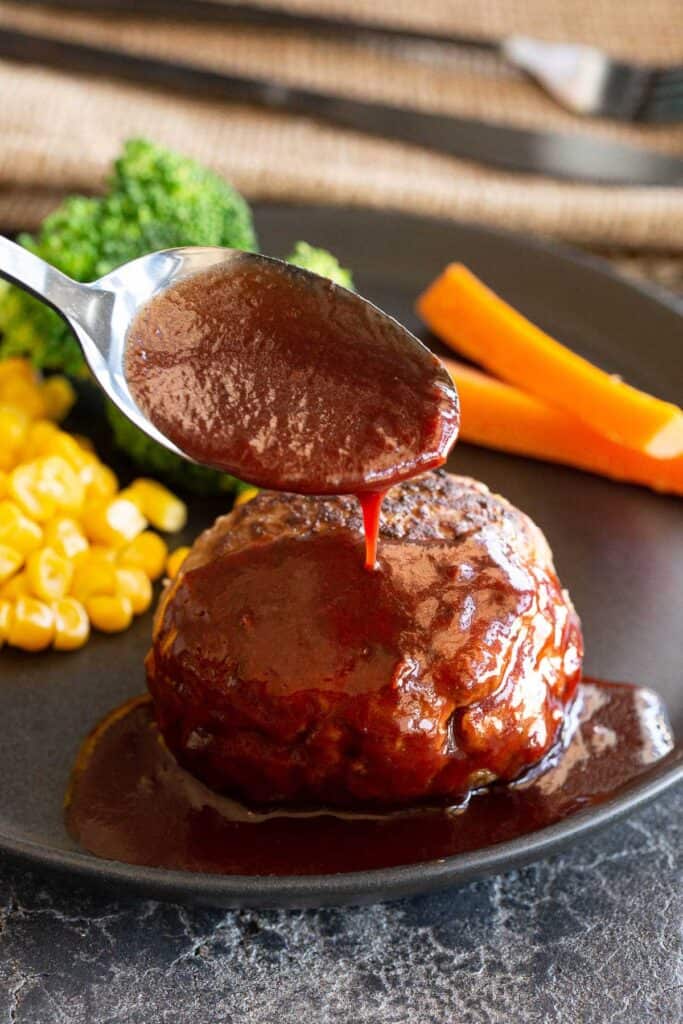 A spoon pours homemade sauce over a hamburger steak.