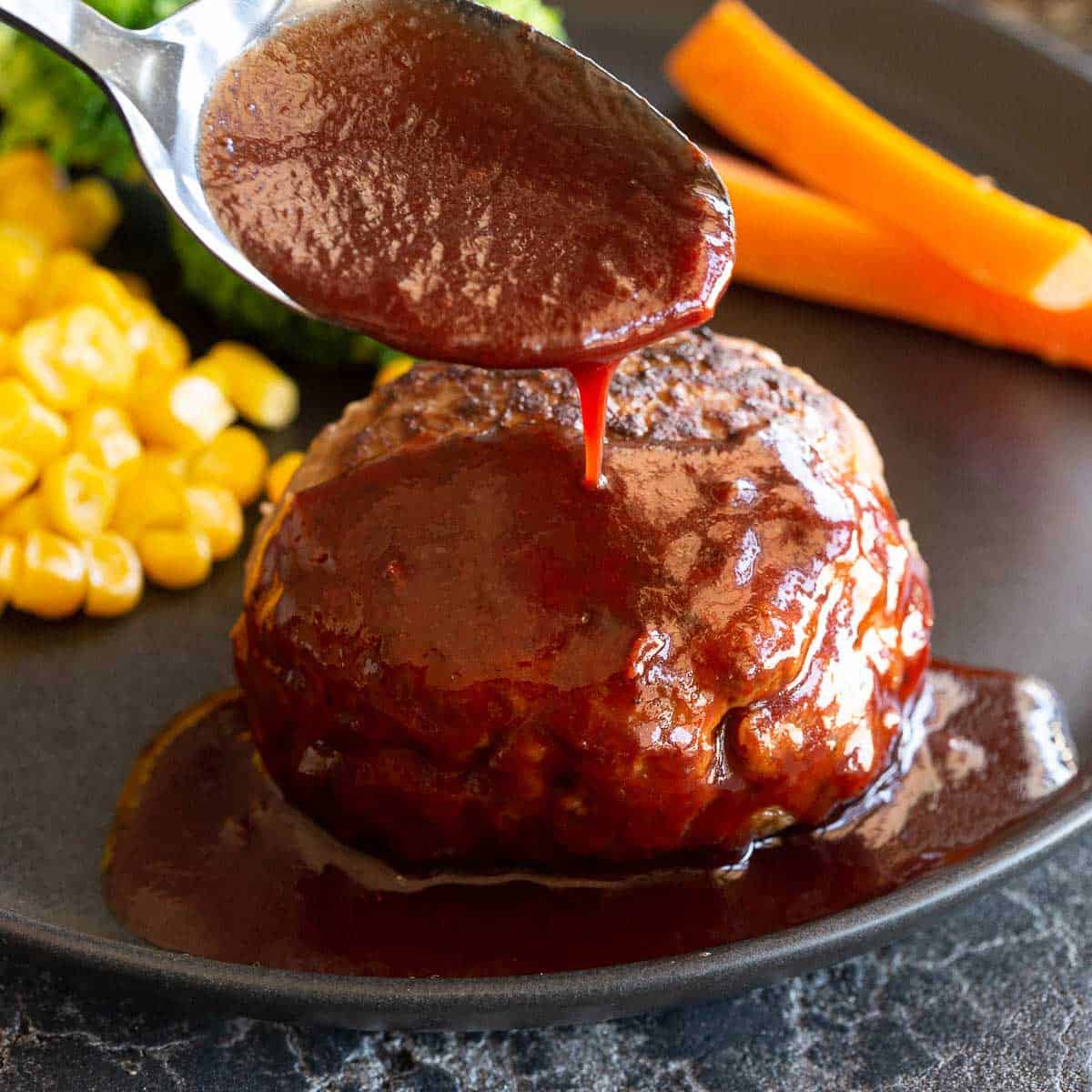 A spoon pours homemade demi-glace sauce over a hamburg.
