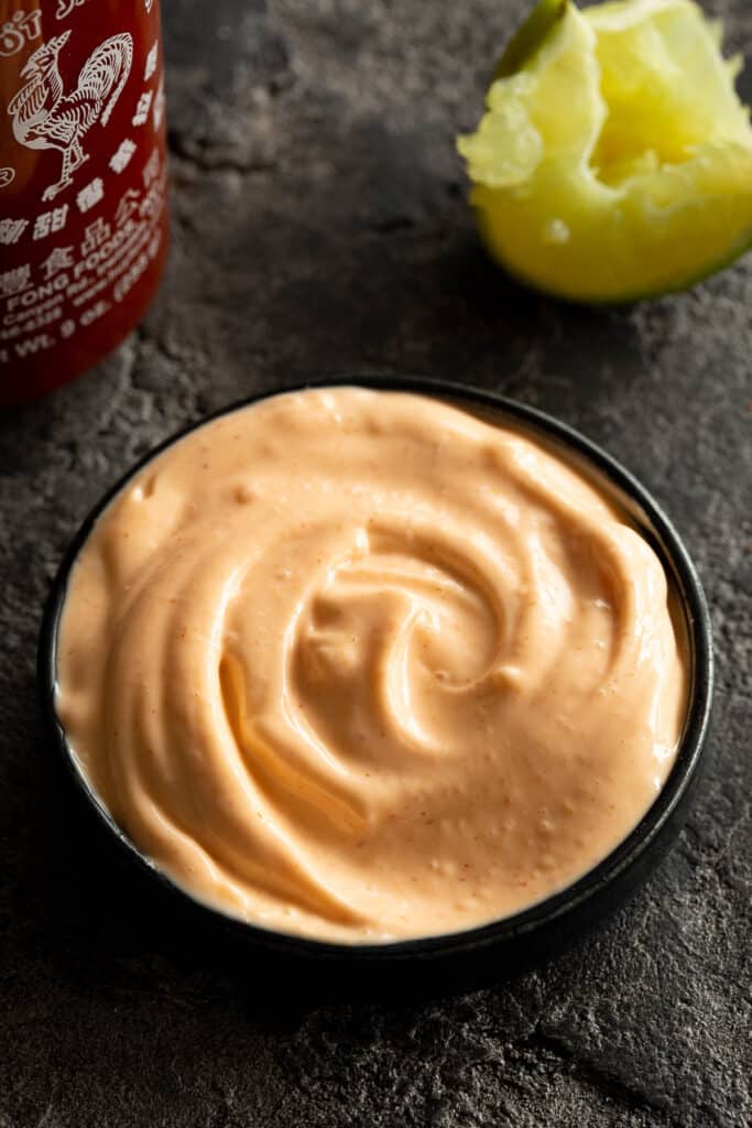 A round dish filled with sriracha aioli, with a squeezed lime wedge nearby.