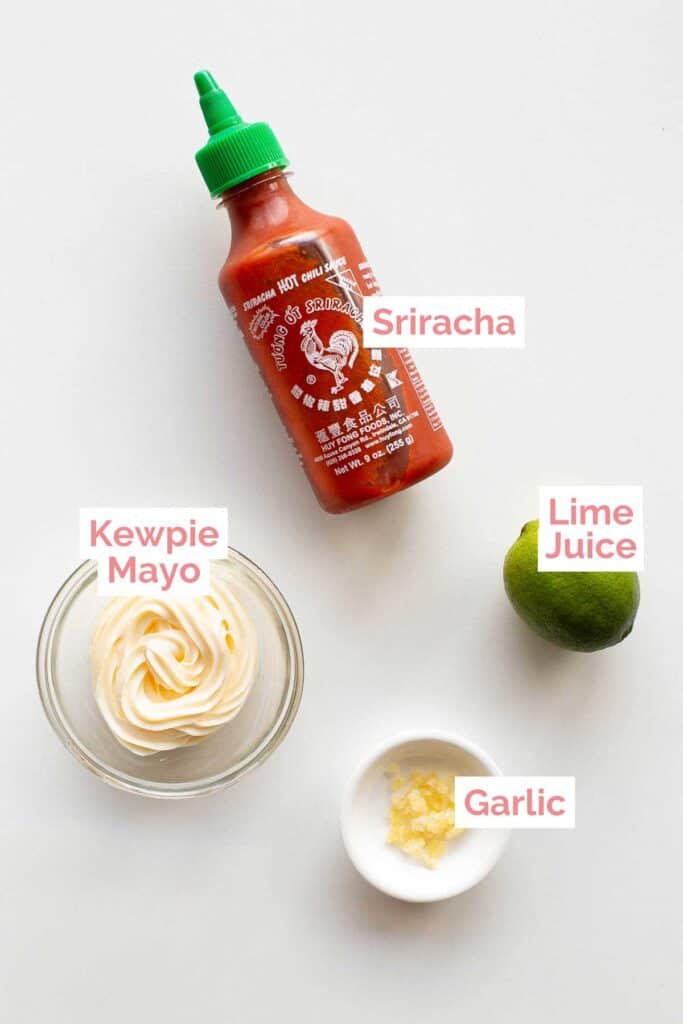 Ingredients laid out for sriracha aoiloi, including sriracha, kewpie mayo, chopped garlic and lime.