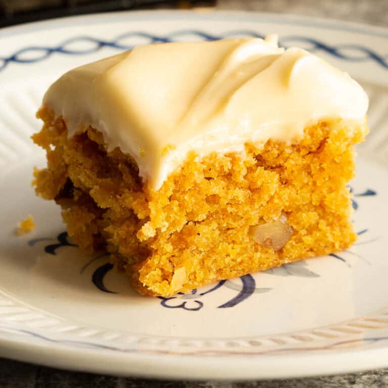 A small square piece of carrot cake on a white plate.