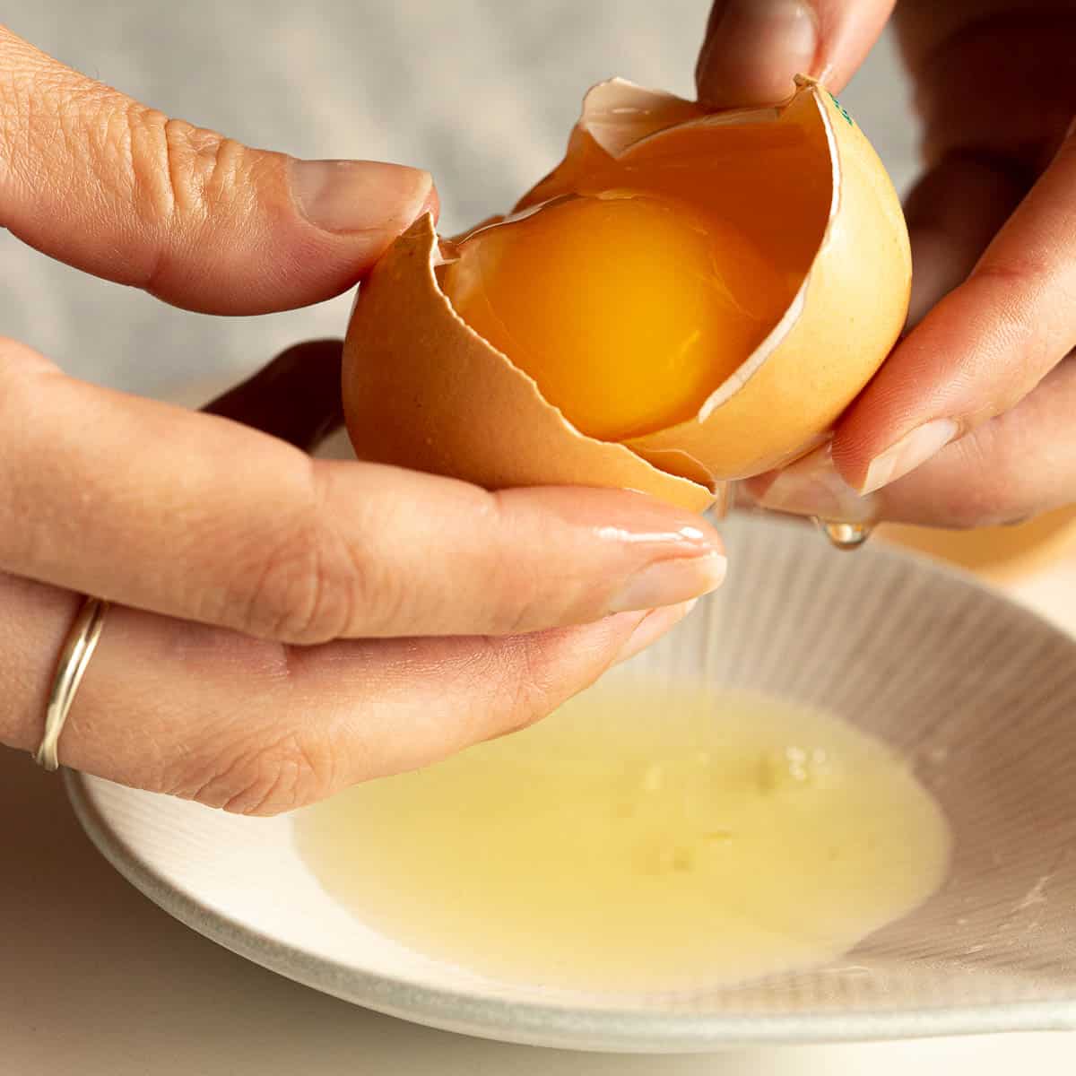 An egg yolk is held in it's shell, while the egg white drops into the dish below.