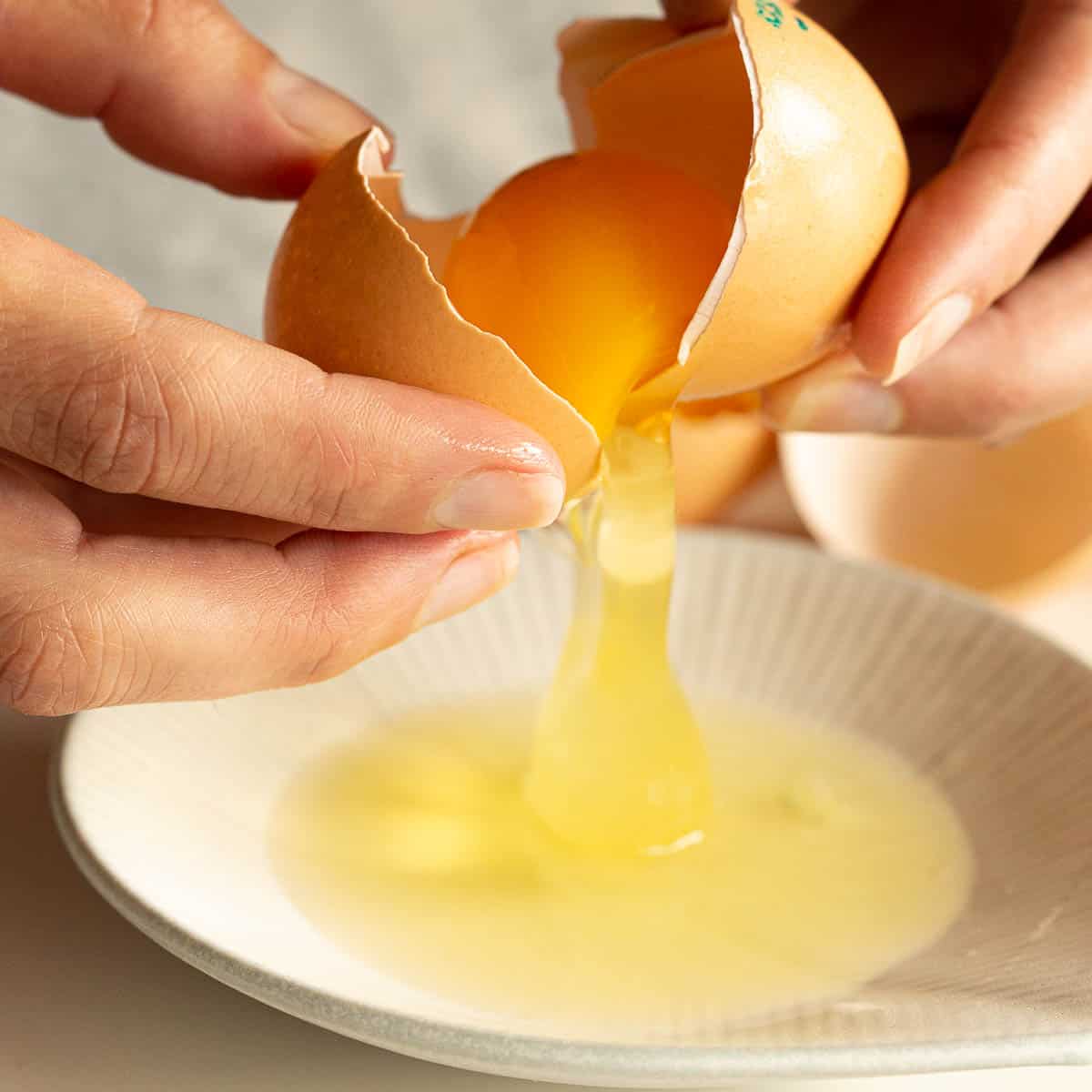 The yolk is being split from the egg white using the shell.