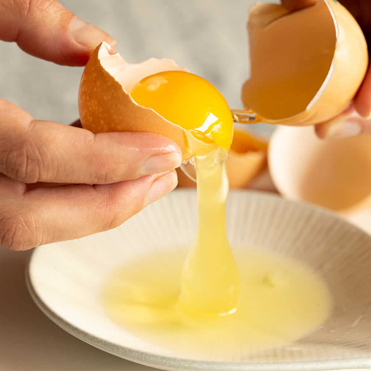 The egg white falls from the egg shell into a dish.