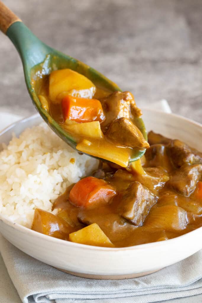 A green spoon places curry into a white bowl.