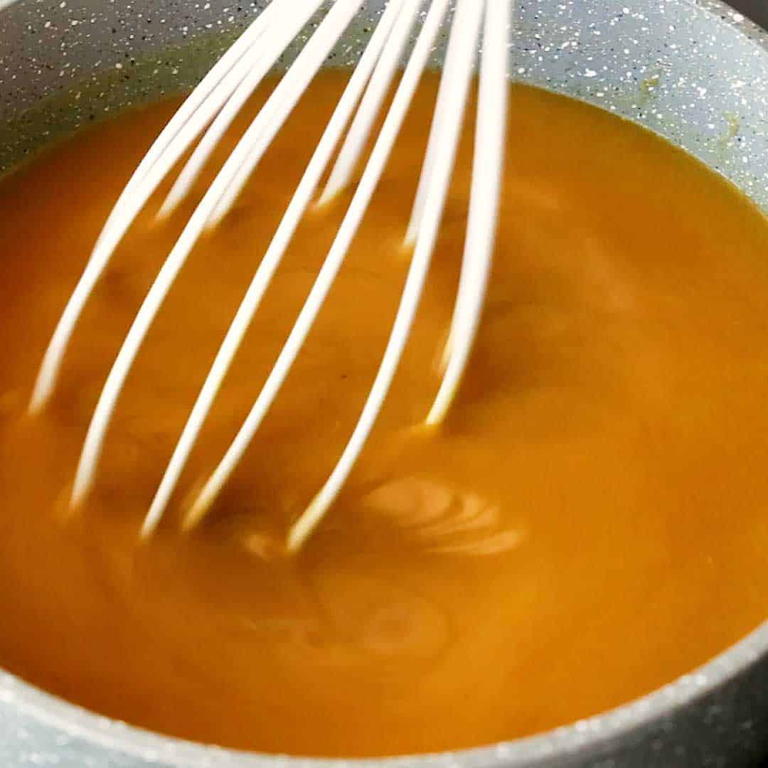 A whisk stirs the thickened curry sauce.