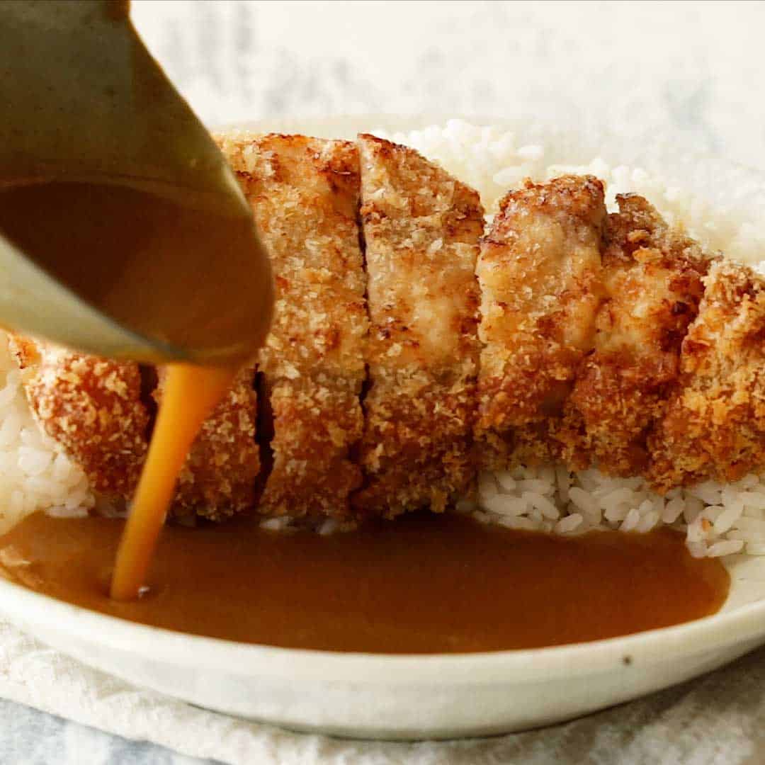 A ladle spoons curry sauce over the tonkatsu.