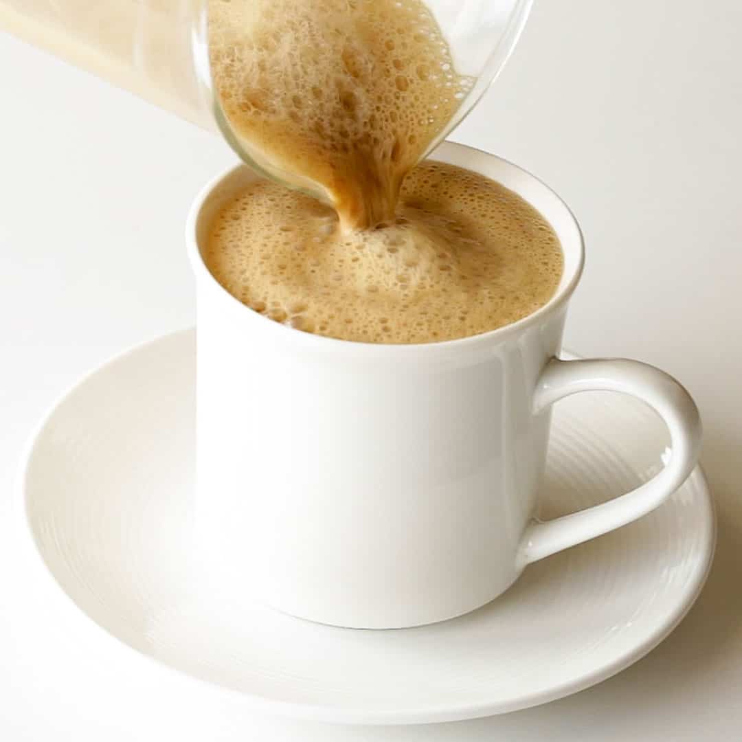 Pouring the finished kopi tarik into a white serving mug.