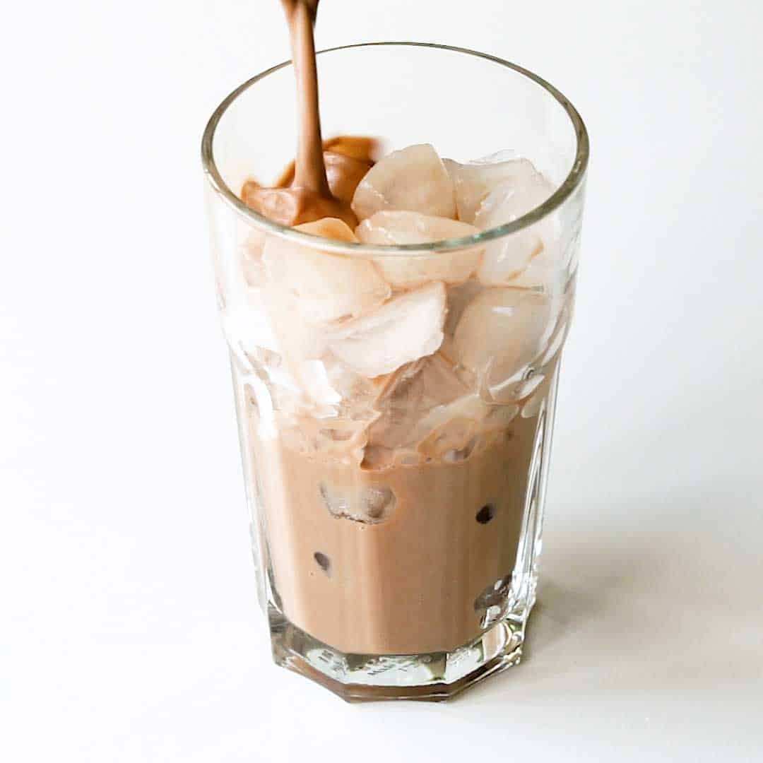 Pouring hot milo into a glass full of ice.