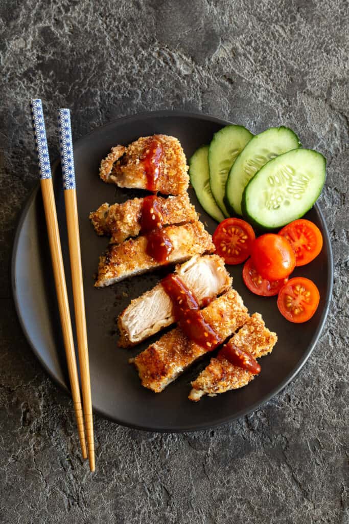 A tonkatsu sliced on a plate with vegetables and chopsticks.