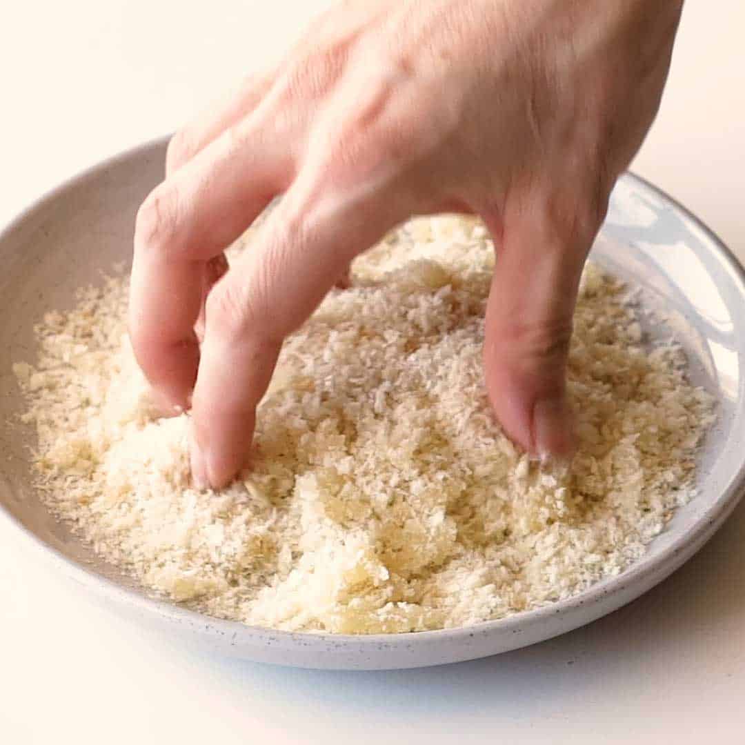 A hand mixes oil and panko crumbs.