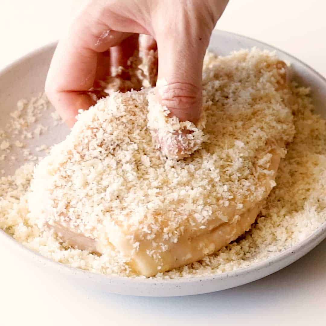 A pork cutlet is coated in panko crumbs on a plate.