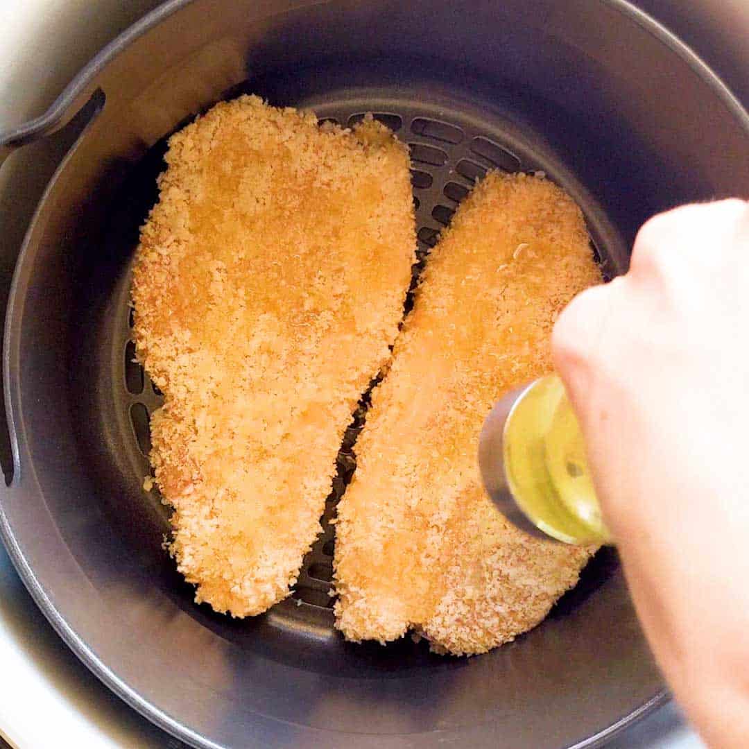 Oil is drizzled over the tonkatsu in an air fryer.