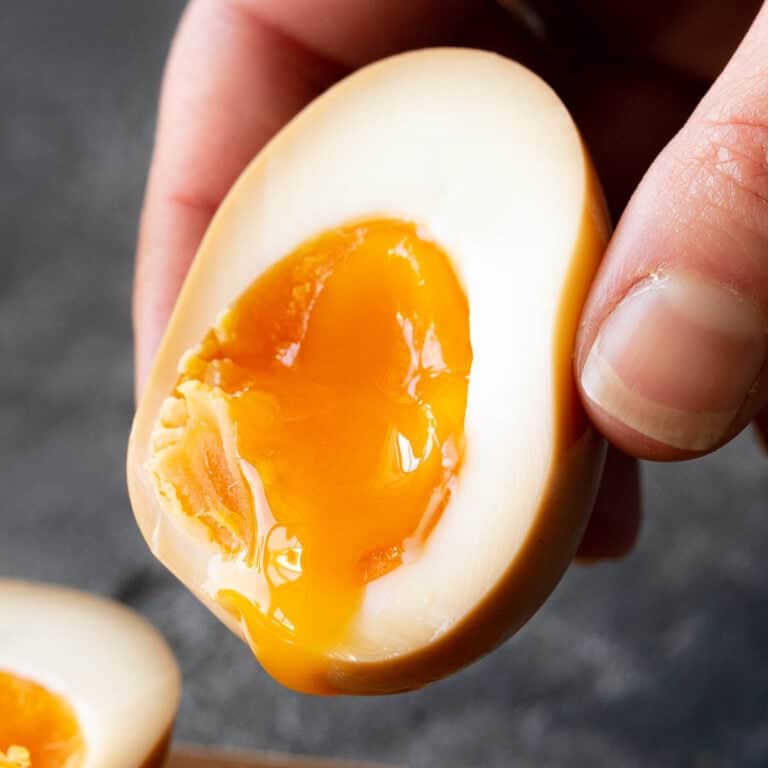 A hand holds half a ramen egg with a soft yolk centre.