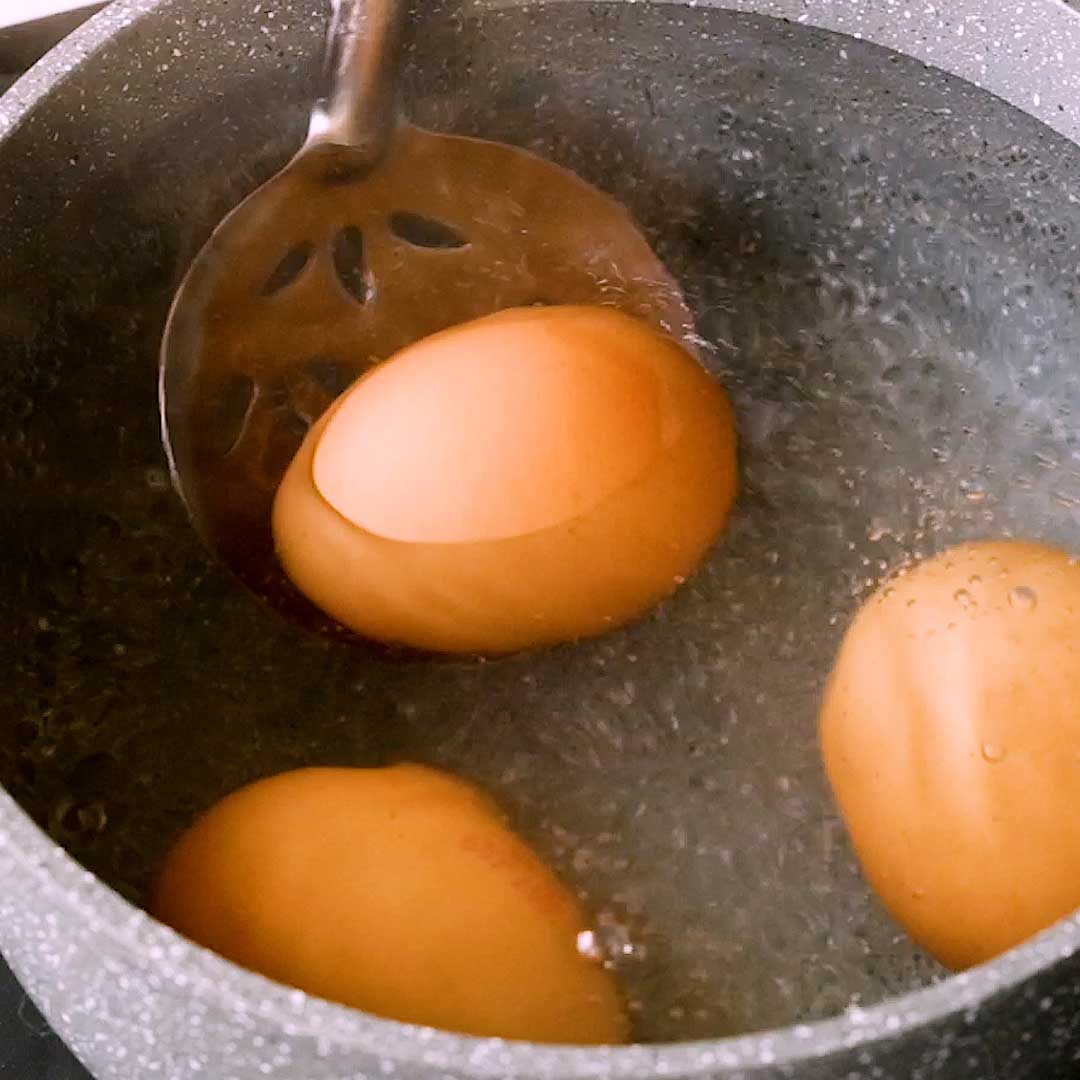 Gently placing cold eggs from fridge in boiling water.