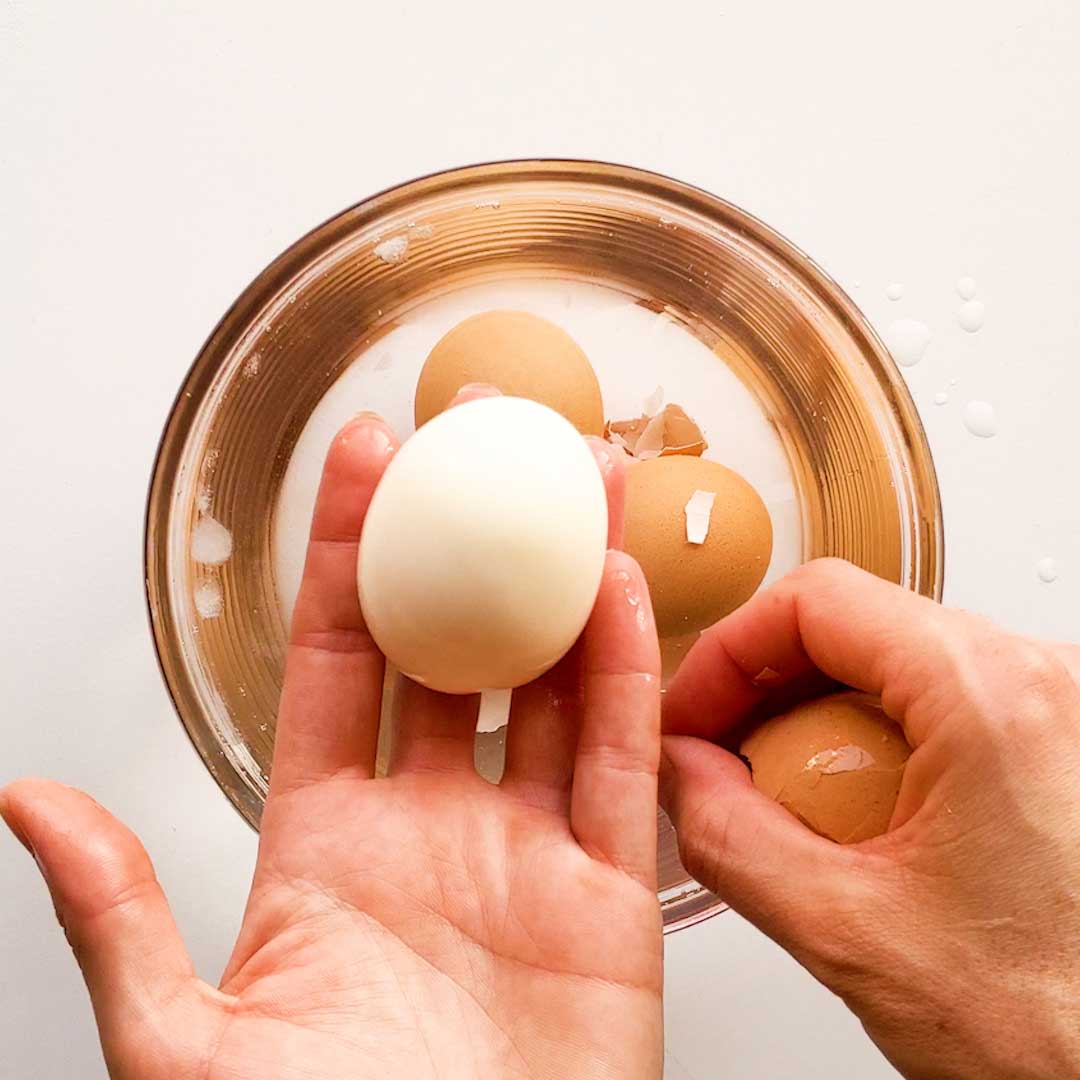 A hand is deshelling the soft boiled egg.