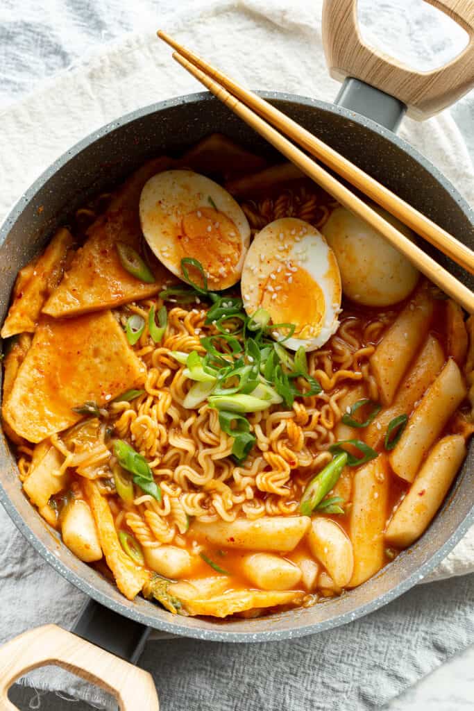 Pot of rabokki with fish cakes, boiled eggs and topped with sesame seeds and spring onion.