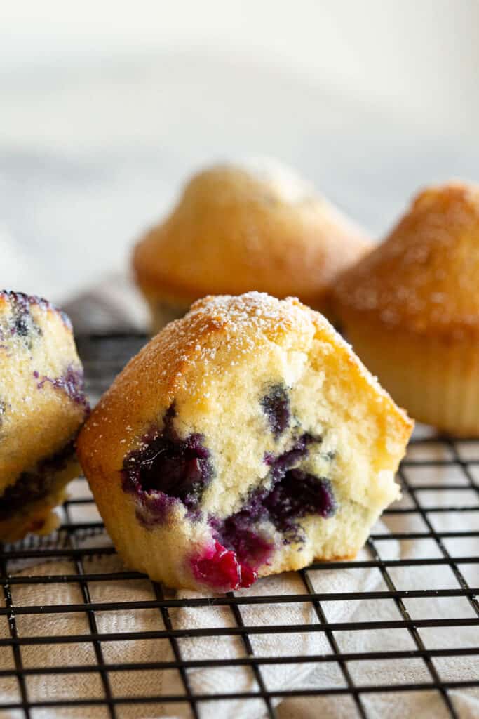 A moist blueberry muffin with a bite taken out on a cooling rack.