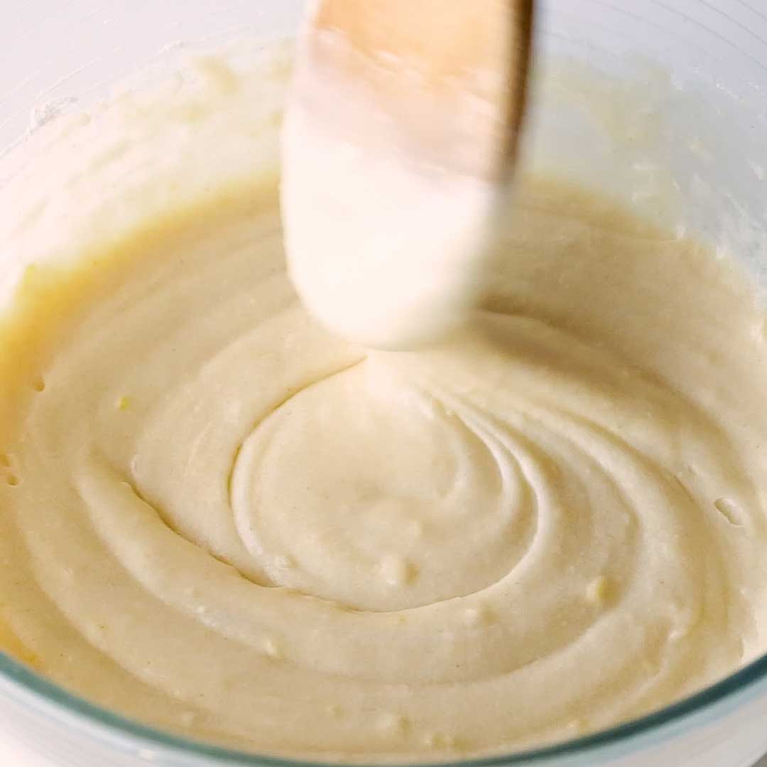 A wooden spoon mixes the smooth muffin batter.