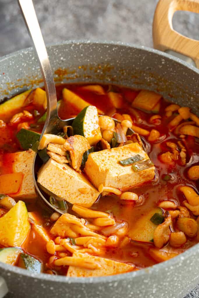 A ladle is full of tofu and zucchini from the gochujang stew.
