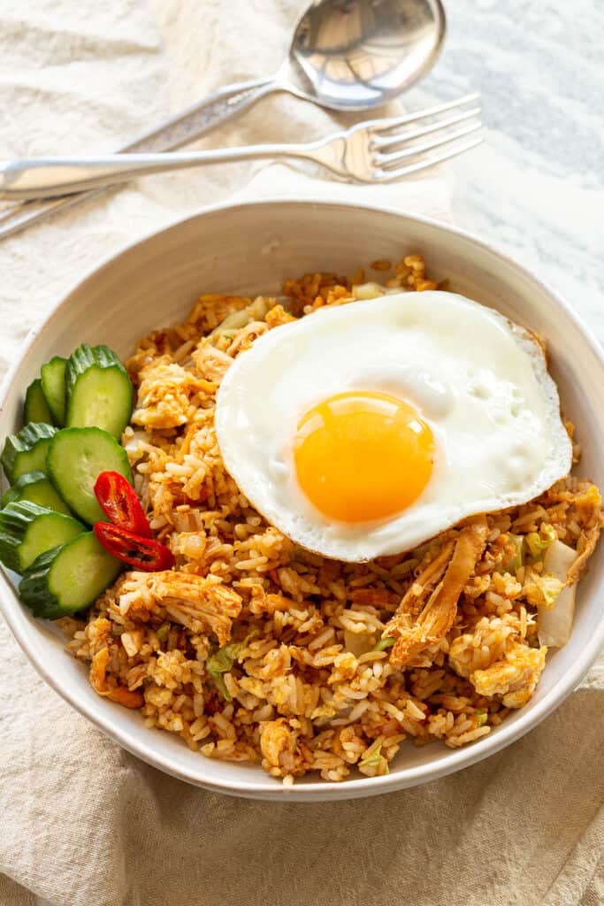 A fresh bowl of Indonesian Fried Rice in a white bowl on linen cloth.